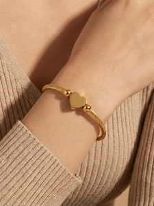 Close-up of a gold-plated heart pendant on a twisted rope chain bangle worn on a wrist
