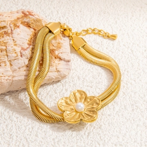 Detail eines goldfarbenen zweilagigen Schlangenarmbands mit Gänseblümchen-Perlenanhänger
