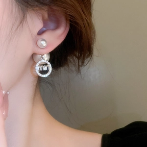 Detailed view of silver needle pearl earrings with letter design worn by model