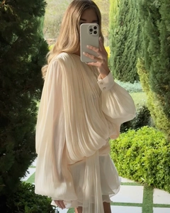 Detail of beige puff sleeve pleated dress with lightweight fabric texture in a garden setting