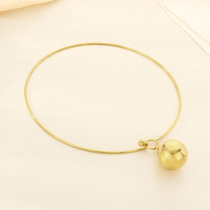 Gros plan d'un pendentif boule dorée lisse sur un collier minimaliste en acier inoxydable