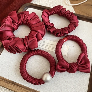 Detail of a 4-piece burgundy satin scrunchie set with pearls and bows in a tray