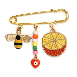 Detail of a gold safety pin brooch with enamel bee, devil's eye and orange slice charms