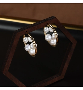 Detailed close-up of golden floral hoop earrings with freshwater pearls on a wooden stand