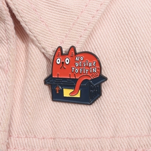Red cat in a black box enamel pin with 'NO DESIRE TO FIT IN' text on pink denim