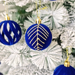 Boules de Noël en velours bleu avec motifs dorés sur un sapin enneigé en gros plan
