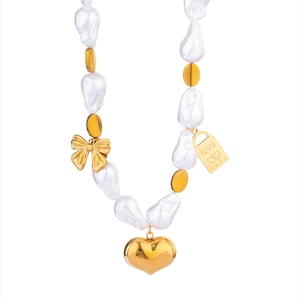 Détails de perles baroques, nœud doré et pendentif cœur gravé d'un message d'amour