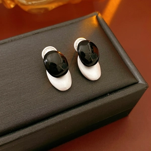 Detail of oval black polished stone and white matte stud earrings on jewelry box