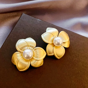 Detailed close-up of golden brushed flower earrings with white pearl center on silk