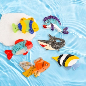 Detailed overhead view of six colorful fish-shaped acetate hair claws on a textured stone