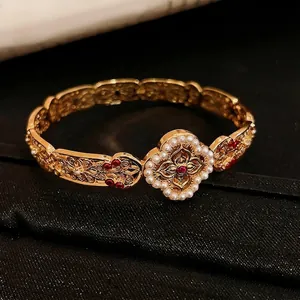 Elegant gold vintage bangle featuring intricate cutouts with red rubies and pearls