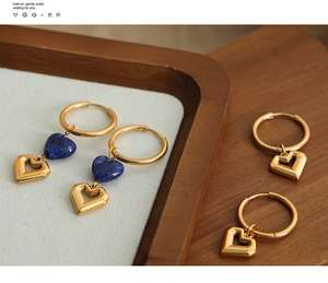 Detailed close-up of gold hollow heart earrings with blue stone on wooden tray