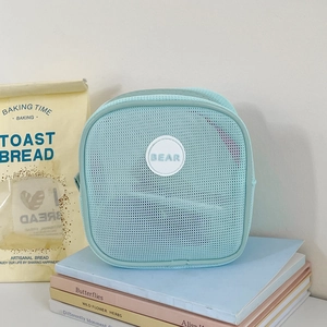 Close-up of mint green mesh makeup bag with BEAR logo on pastel books background