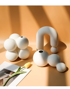 Drei minimalistische mattweiße Keramikvasen in geometrischen Formen auf warmem Hintergrund