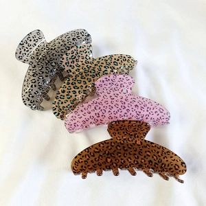 Close-up of four leopard print hair claws in grey yellow pink and brown on white fabric