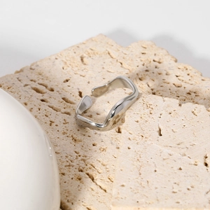 Dettaglio di anello in metallo argento a forma di onda irregolare su base in pietra beige