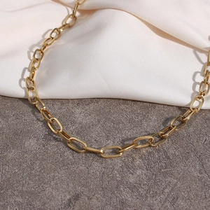 Dettaglio della collana a catena Figaro dorata su seta bianca e sfondo in cemento