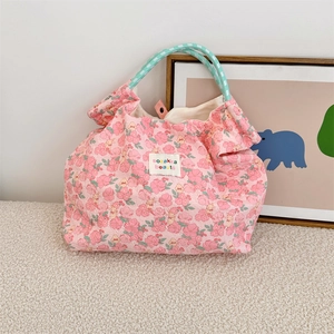 Detailed texture of pink floral tote bag with green woven handles and brand label