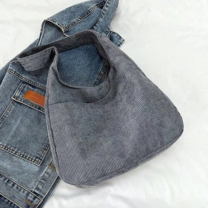 Detailstruktur der grauen Cord-Hobo-Tasche auf weißem Bettzeug mit Jeansjacke