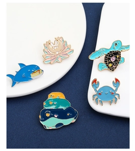 Close-up of enamel pins showing cartoon shark, turtle, and crab on display pedestals