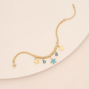 Detail of gold snake chain bracelet with star charms and blue beads on ceramic plate