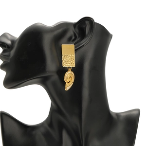 Golden geometric earrings with white spiral pendant shown on a black model profile