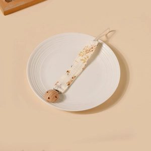 Détail de l'attache-tétine en coton fleuri avec clip en bois de hêtre sur assiette