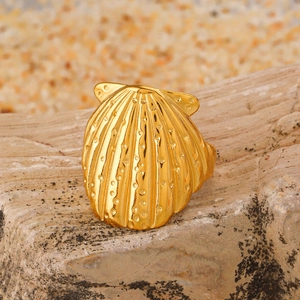 Gold scallop shell ring on textured rock base with a warm summer beach vibe