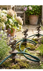 Detail of vintage cast iron bird hose guide stakes placed in a blooming garden landscape