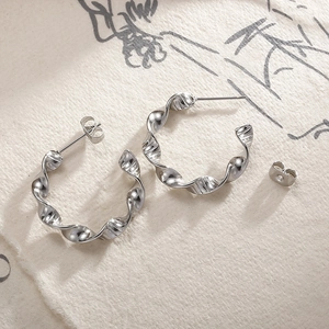 Detail view of silver wavy twist hoop earrings on minimalist textured artistic paper