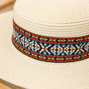 Detail of flat-top straw sun hat with bohemian geometric pattern ribbon and weave texture