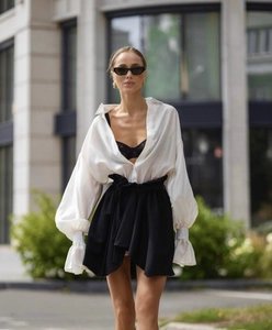 Detail of a white V-neck lantern sleeve shirt paired with a black high-waisted belted skirt
