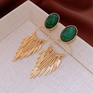Detail view of vintage oval green stone earrings with golden tassel on beige background