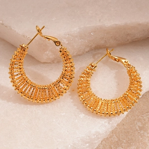 Detail shot of golden hollow mesh woven geometric hoop earrings on stone surface