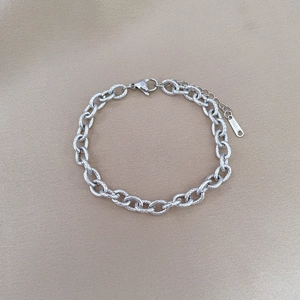 Macro detail of a vintage silver-colored stainless steel chain link bracelet on fabric
