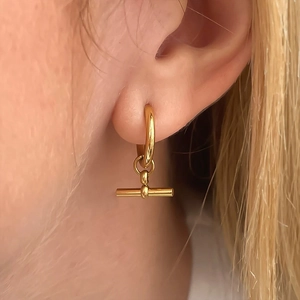 Gros plan d'une boucle d'oreille huggie dorée avec barre en T portée à l'oreille