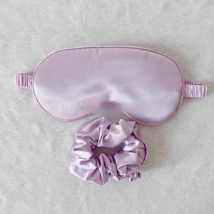 Detail view of lavender silk sleep mask and hair scrunchie set on white plush background