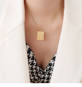 Detail of a vintage 18k gold plated checkered square pendant necklace worn by a model