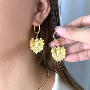 Gros plan de boucles d'oreilles cœur dorées texturées portées par un mannequin