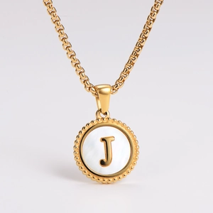 Detail shot of golden necklace with a white shell pendant and embossed letter J inlay