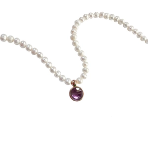 Detail of white pearl necklace featuring a round purple gemstone pendant on white background