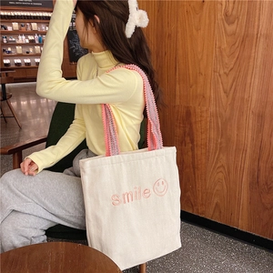 Close-up of cream canvas tote bag with pink smile embroidery and woven shoulder strap