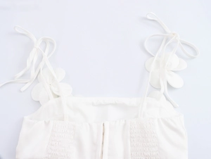 Detail eines weißen Camisoles mit 3D-Blumen, gesmoktem Stoff und zentralem Reißverschluss