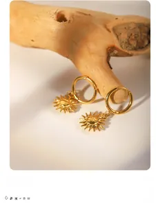 Close-up of 18k gold-plated sun face charms on hoop earrings with vintage texture