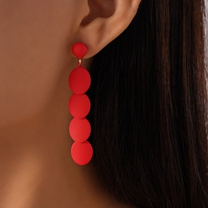 Close-up of long matte red geometric oval earrings worn by a model for a stylish look