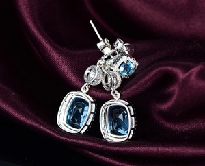 Macro shot of cushion cut blue gemstone drop earrings on purple velvet background