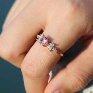 Macro shot of a gold ring with round pink gemstone and marquise side stones on a finger