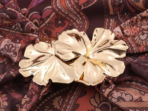 Gros plan d'une boucle métallique dorée en forme de fleur sur une robe en tulle paisley