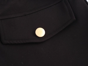 Macro detail of high-waisted black fabric with a polished gold metal button on the pocket