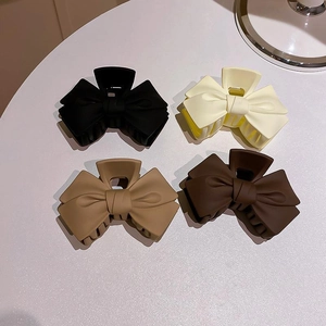 Detailed view of matte bow hair claws in black, cream, khaki, and brown shades